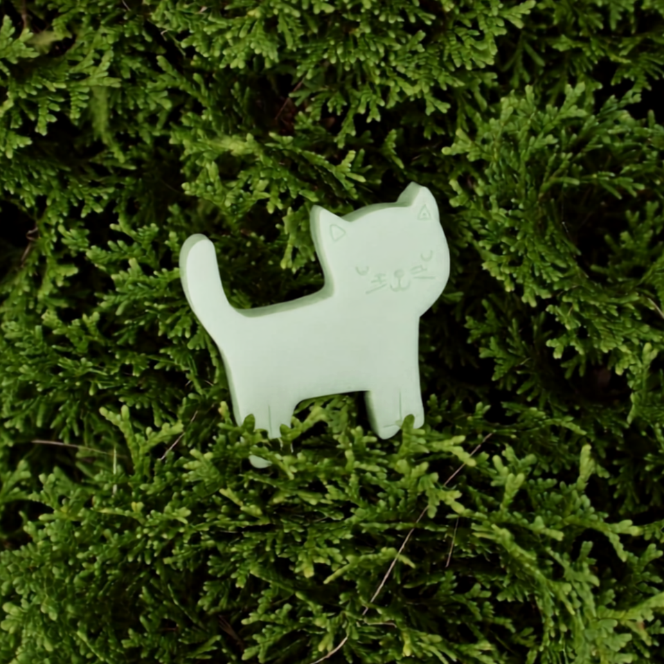A small pale mint-green cat-shaped soap  resting on dense green moss.