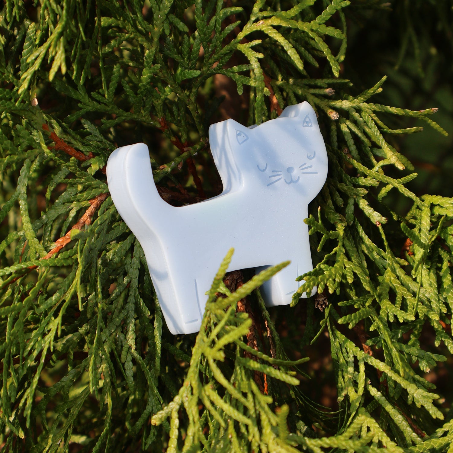 A light blue cat-shaped soap nestled among green pine needles.