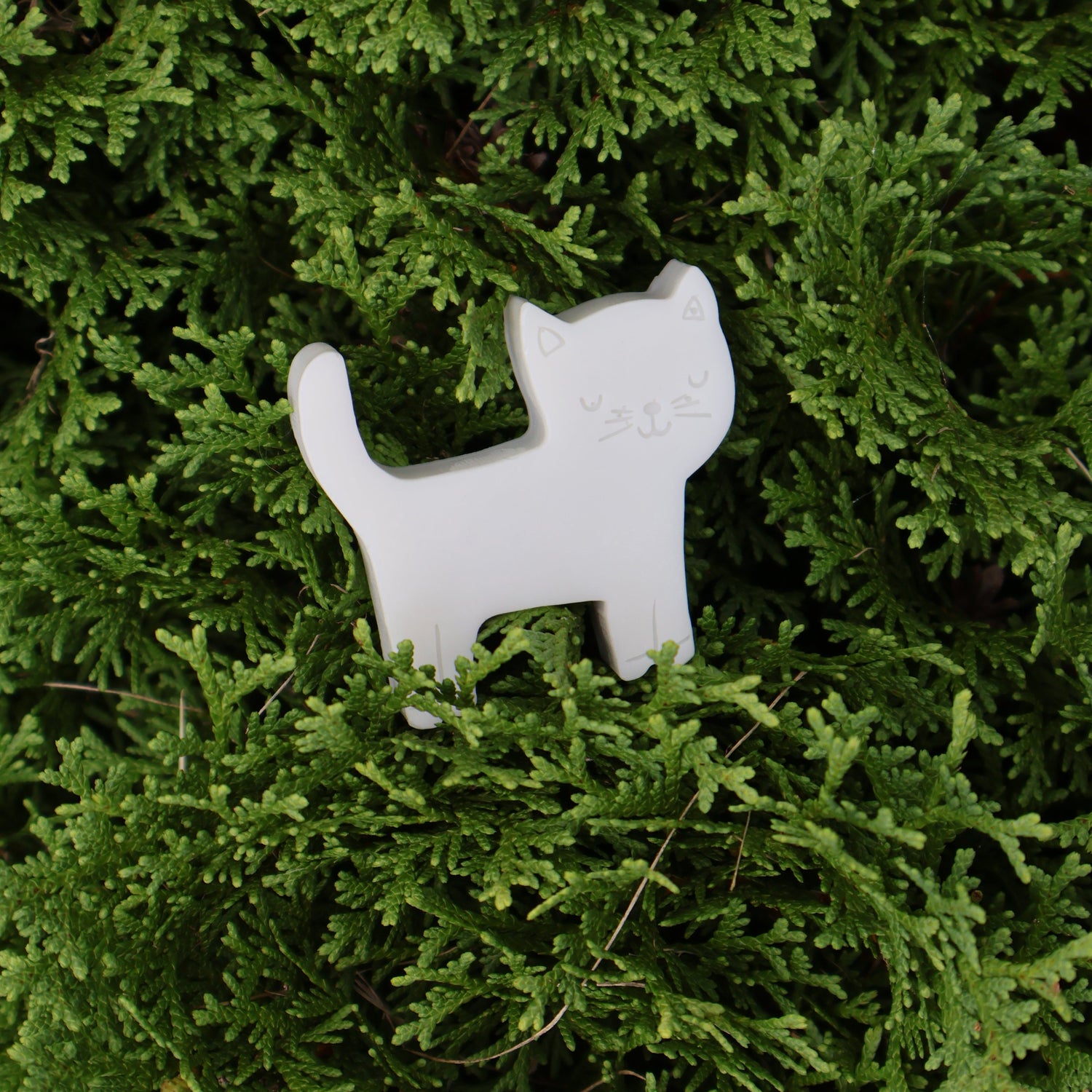 A small grey cat-shaped soap resting on dense green bush.